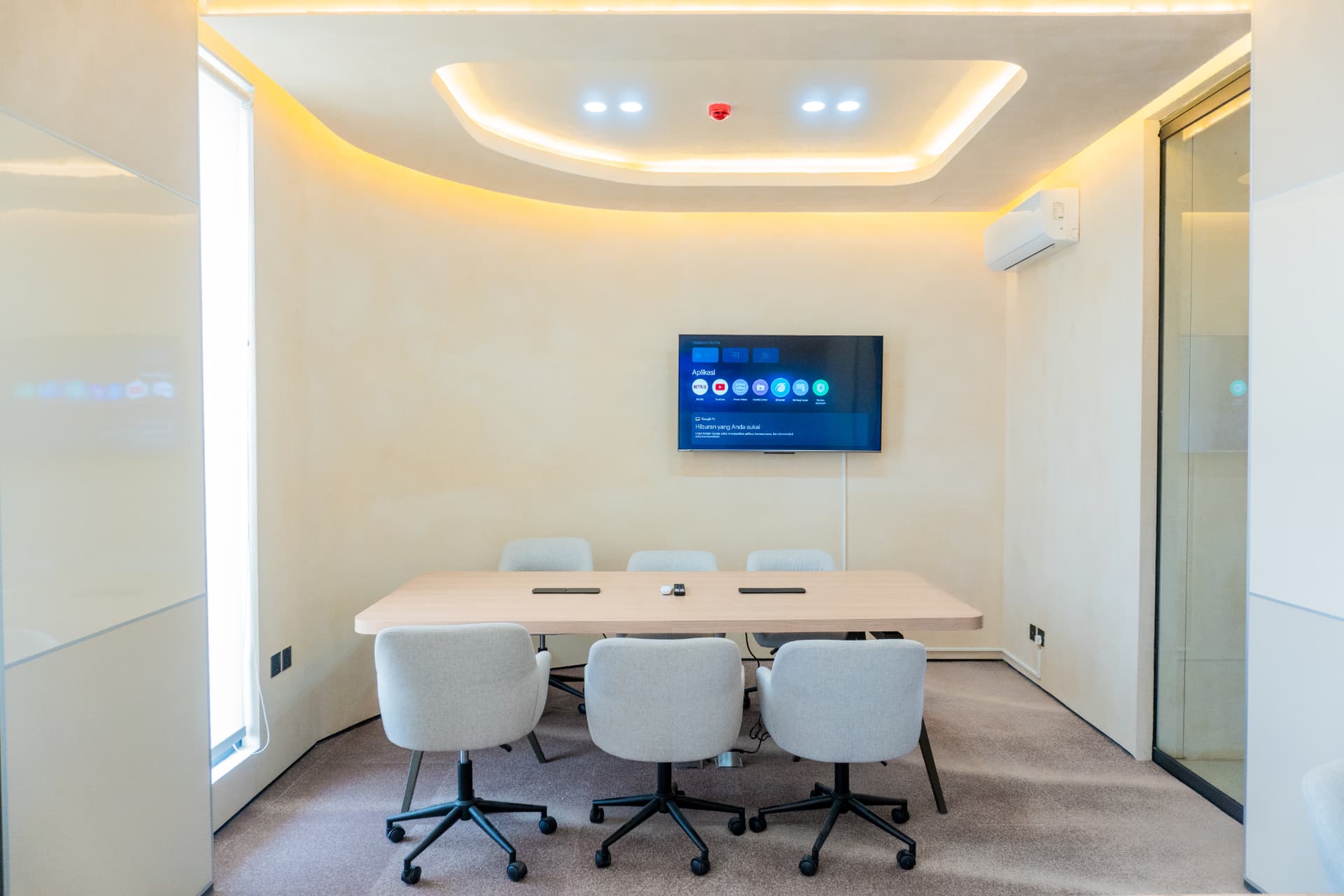 A meeting room at Argil in Pererenan, with grey chairs, a long table and a wall-mounted TV